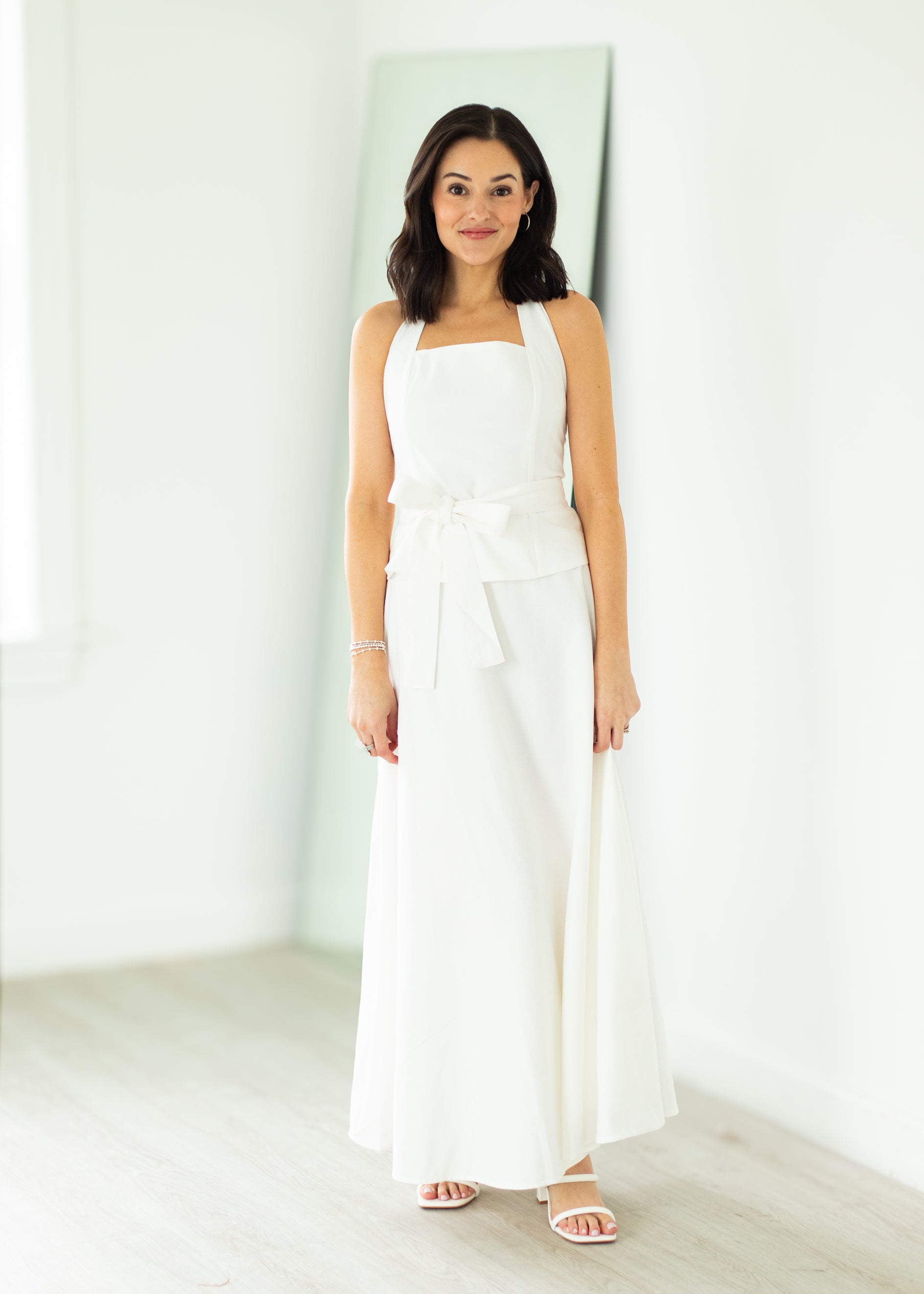 Woman wearing a white halter neck dress with a belt on a beige background

