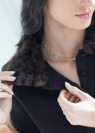 Close-up of a woman wearing a black knit top with a dark brown fur collar, accessorized with a gold chain necklace and bracelet.