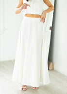 Woman wearing a white halter neck dress with a belt on a beige background

