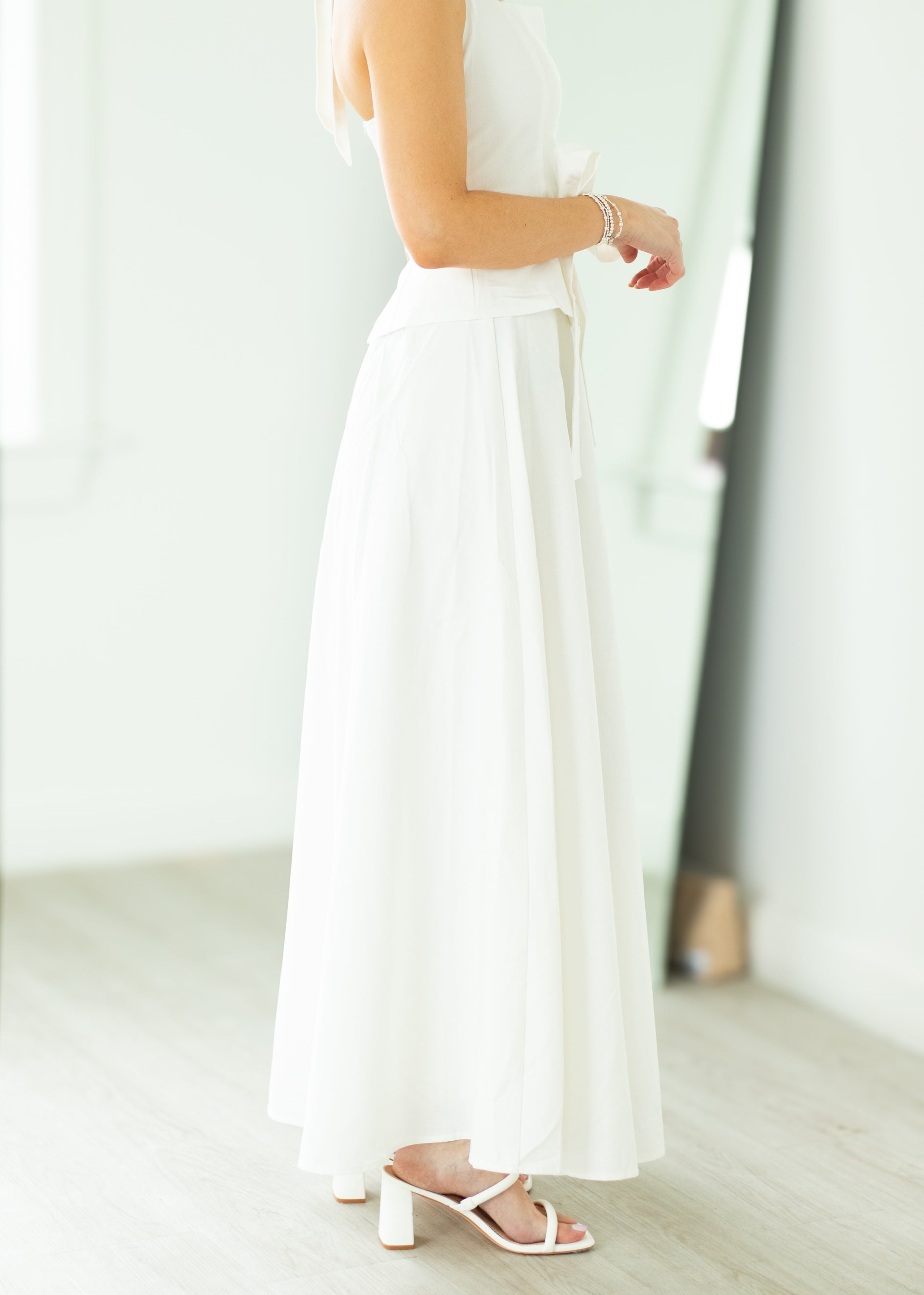 Woman wearing a white halter neck dress with a belt on a beige background

