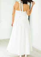 Woman wearing a white halter neck dress with a belt on a beige background

