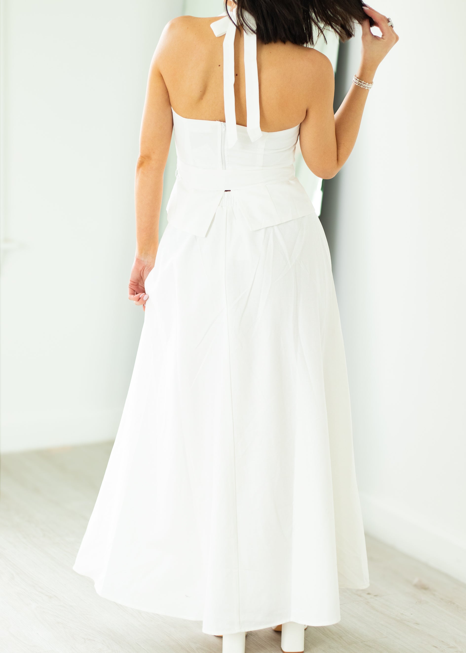 Woman wearing a white halter neck dress with a belt on a beige background

