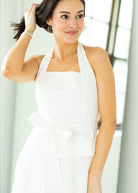 Woman wearing a white halter neck dress with a belt on a beige background

