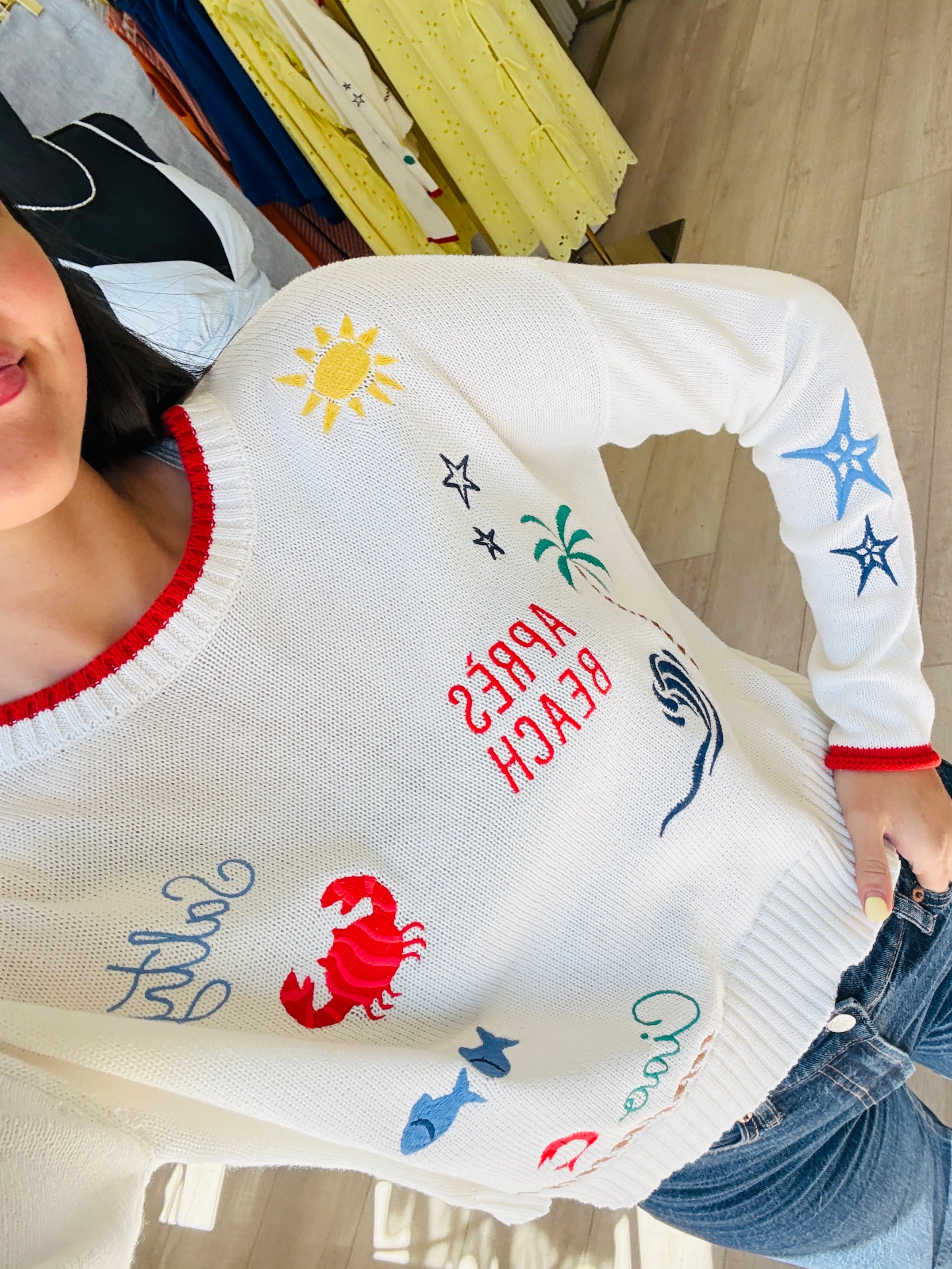 Person wearing a white sweater with colorful beach-themed designs.
