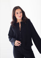 A woman modeling a black long-sleeve button-front top and matching black pants against a plain white studio background.