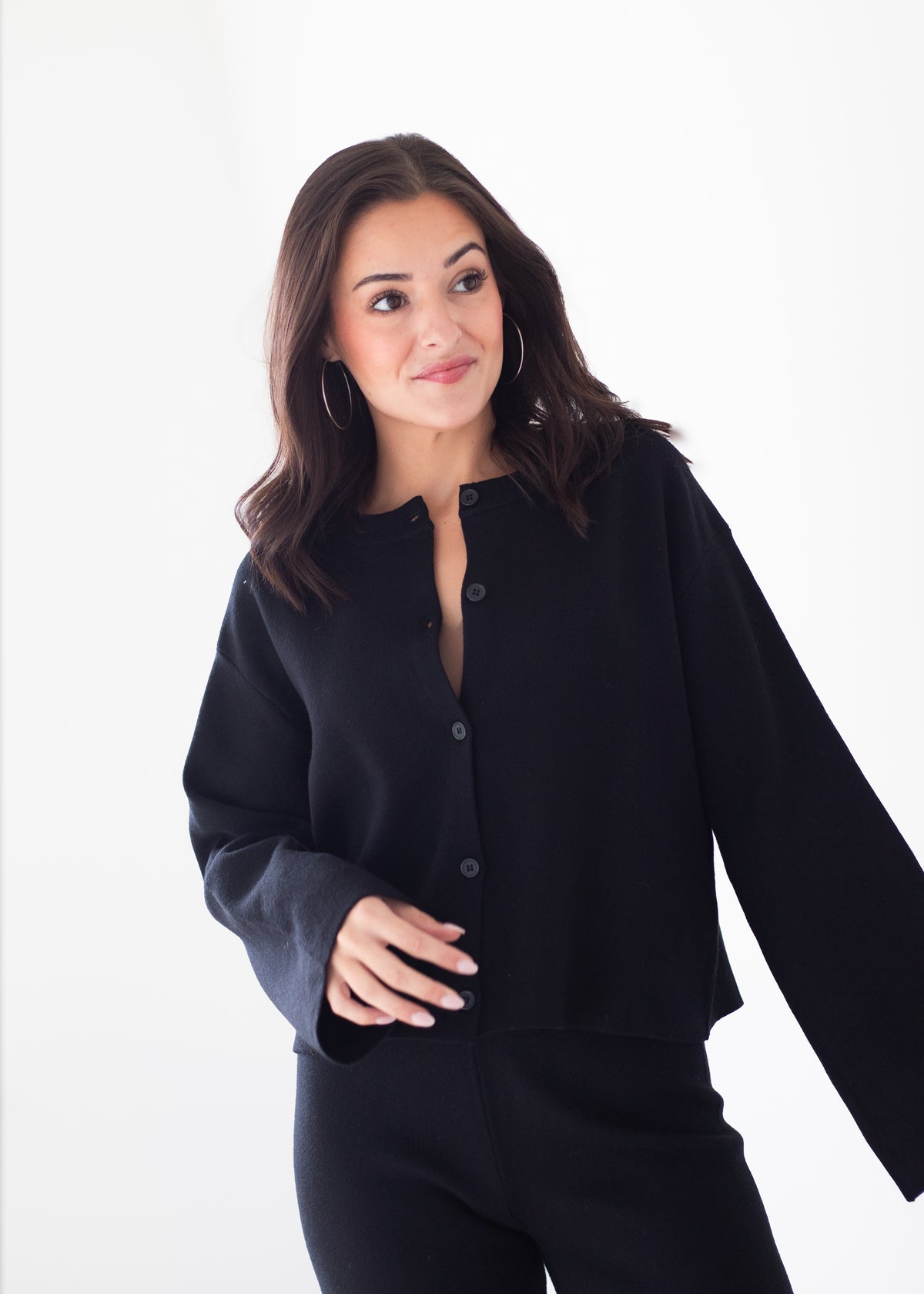 A woman modeling a black long-sleeve button-front top and matching black pants against a plain white studio background.