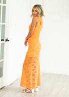 Woman wearing an orange crochet dress against a neutral background

