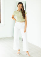 Woman wearing a green short-sleeve cardigan and blue jeans against a neutral background

