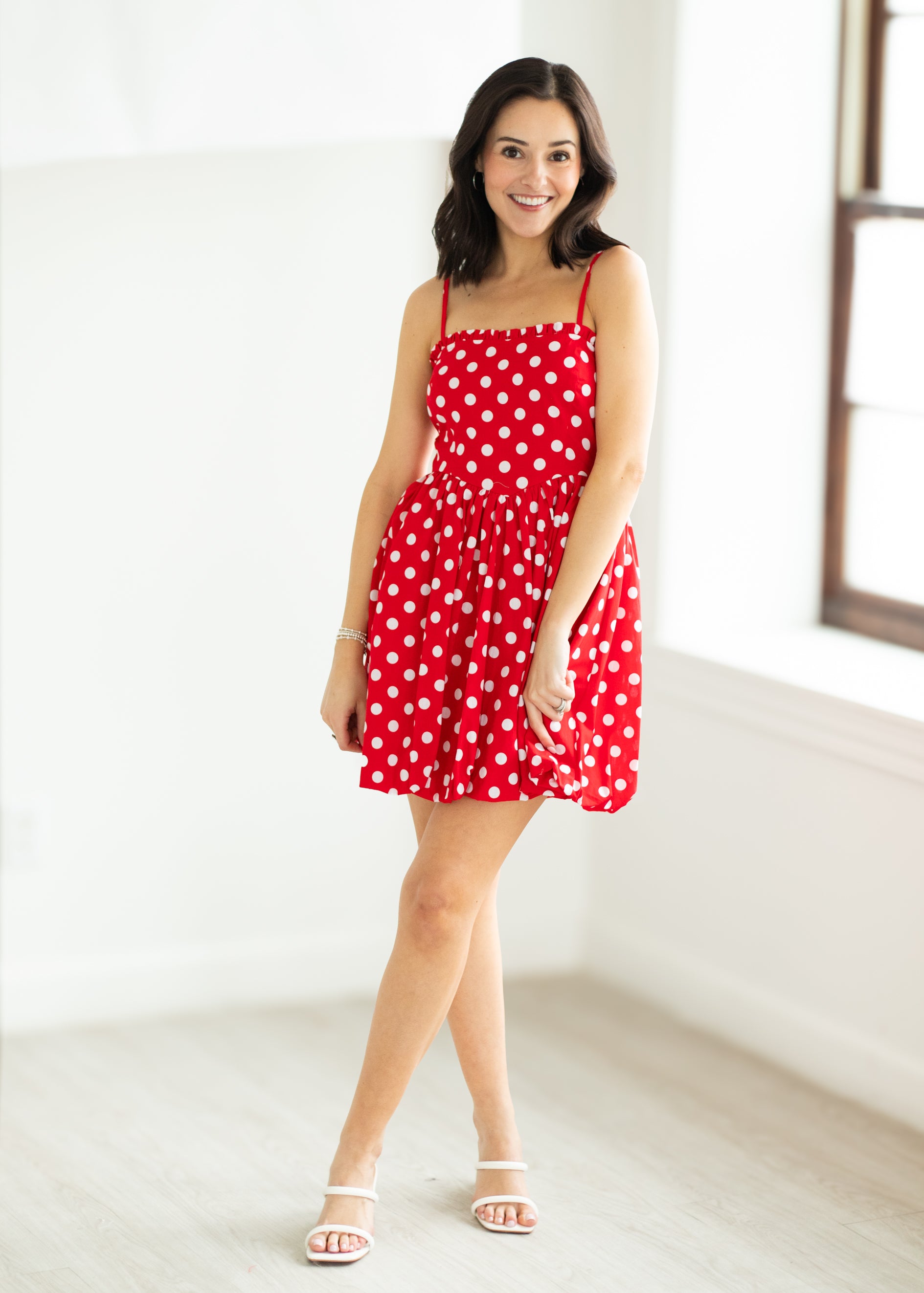 Woman wearing a red polka dot dress with sunglasses on a beige background

