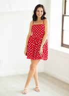 Woman wearing a red polka dot dress with sunglasses on a beige background

