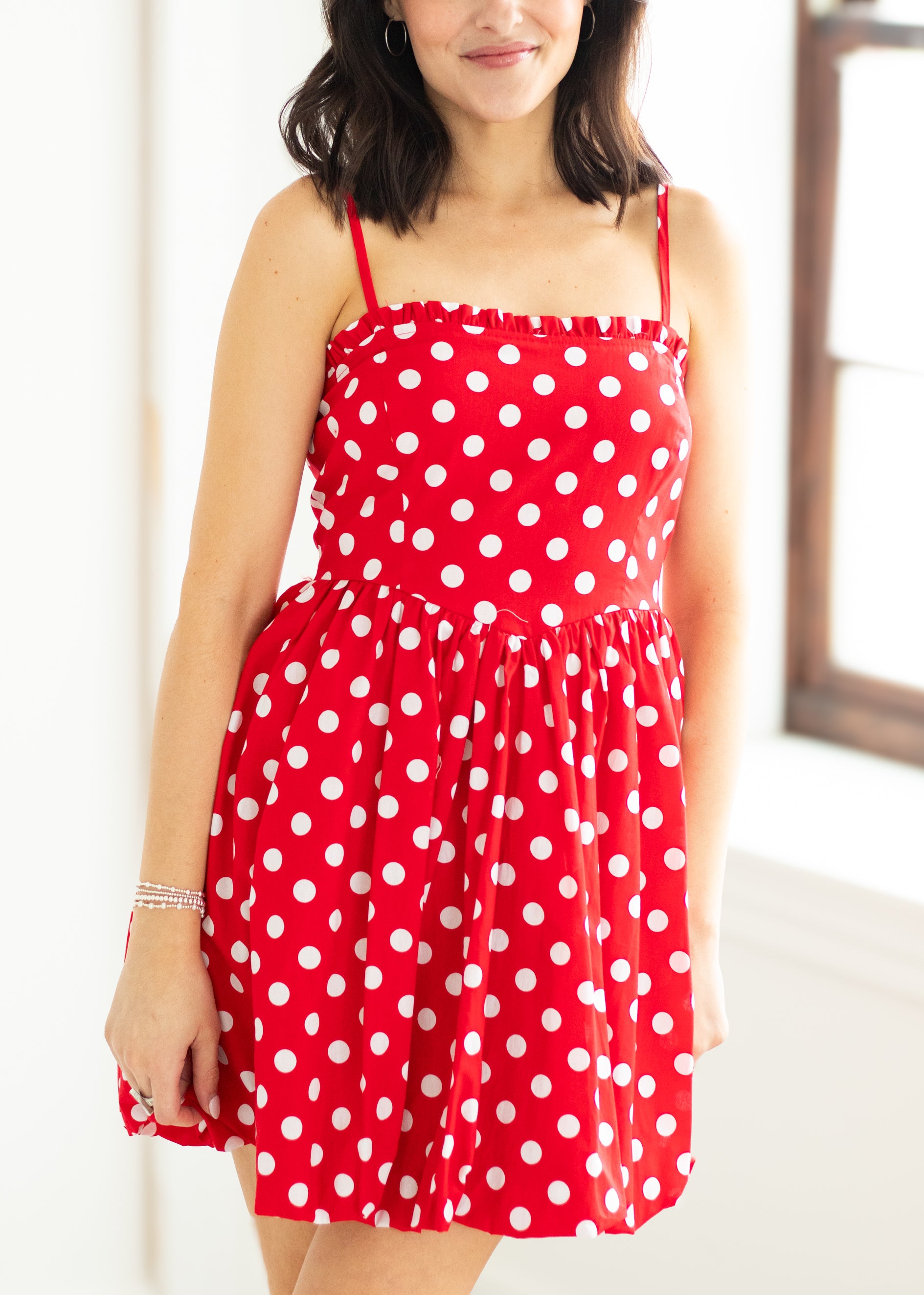 Woman wearing a red polka dot dress with sunglasses on a beige background

