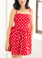 Woman wearing a red polka dot dress with sunglasses on a beige background

