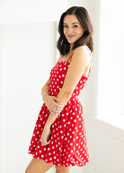 Woman wearing a red polka dot dress with sunglasses on a beige background

