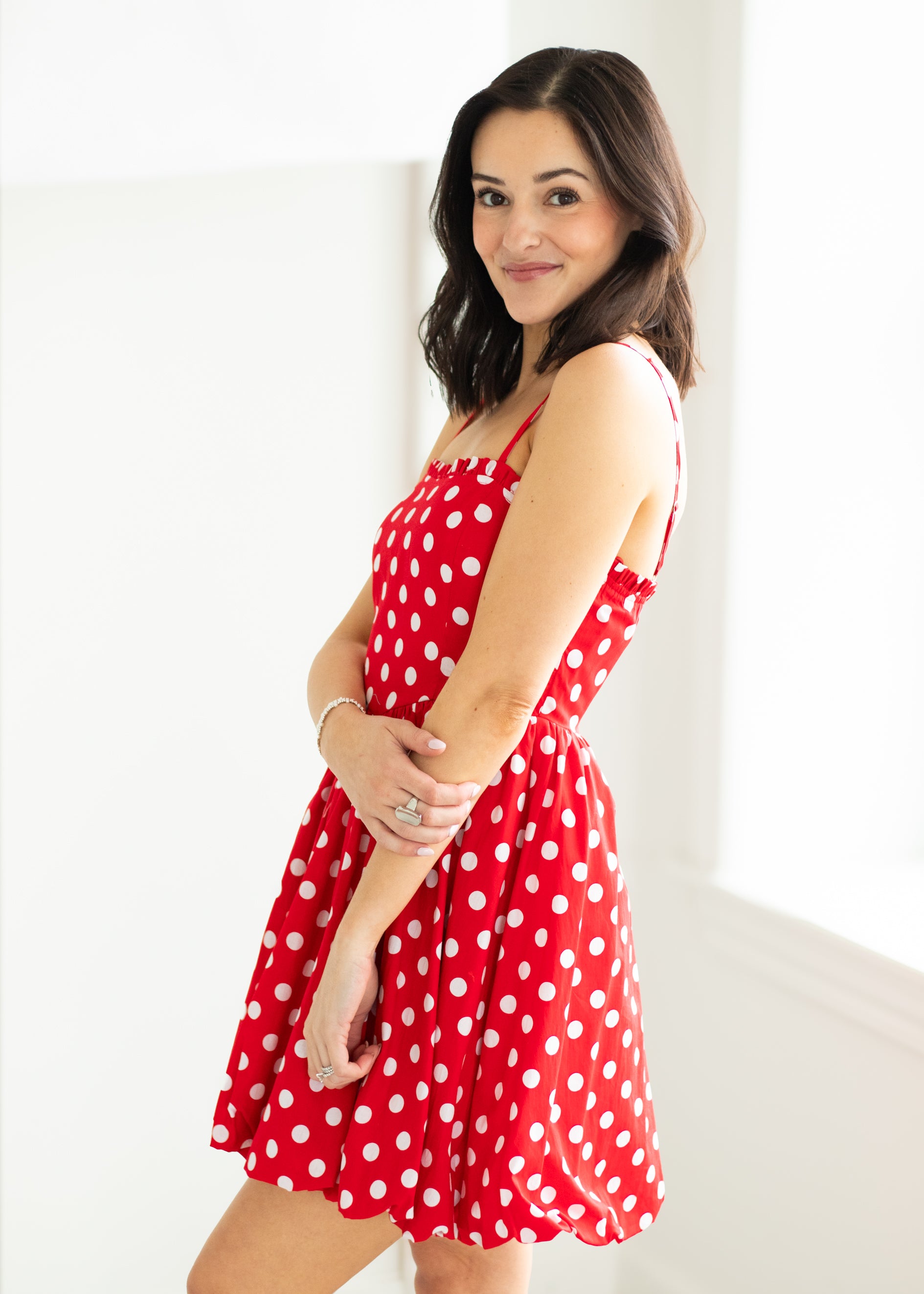 Woman wearing a red polka dot dress with sunglasses on a beige background

