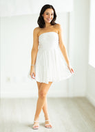 Woman wearing a white strapless dress against a gray background

