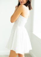 Woman wearing a white strapless dress against a gray background

