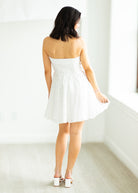 Woman wearing a white strapless dress against a gray background

