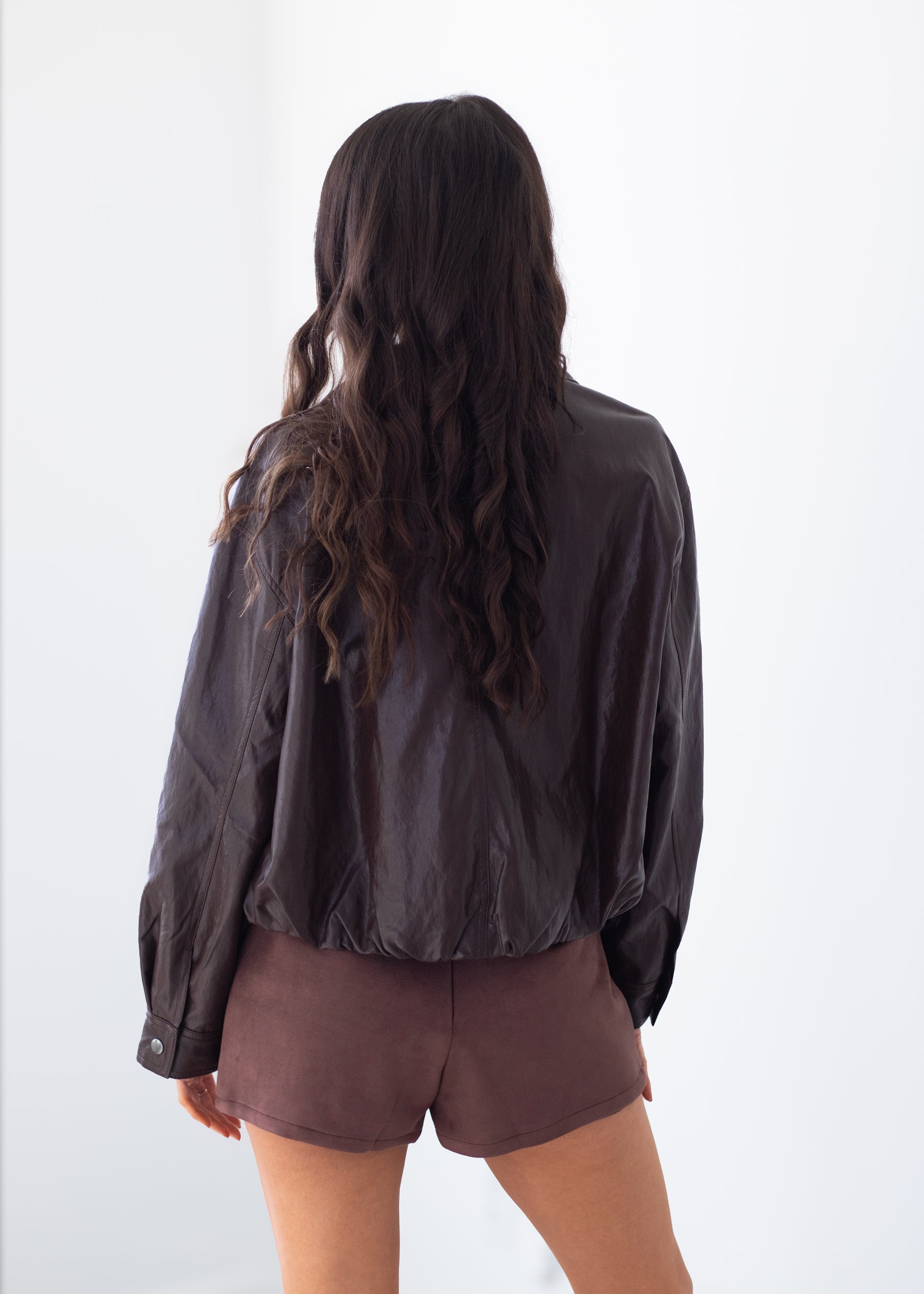 A woman shown from behind wearing a dark brown crinkled long-sleeve jacket and matching brown shorts against a plain white background.