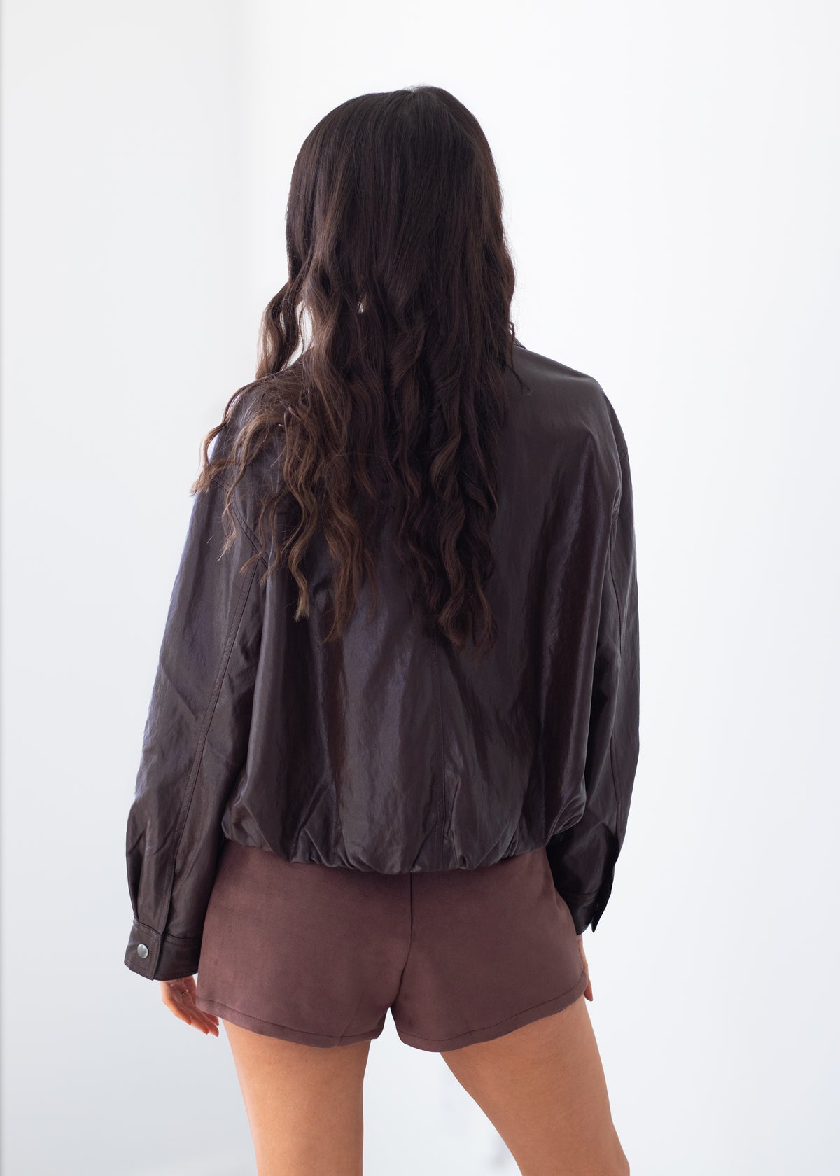 A woman shown from behind wearing a dark brown crinkled long-sleeve jacket and matching brown shorts against a plain white background.