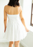 Woman wearing a white strapless dress against a gray background

