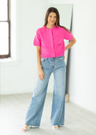 Woman wearing a bright pink cropped cardigan against a beige background

