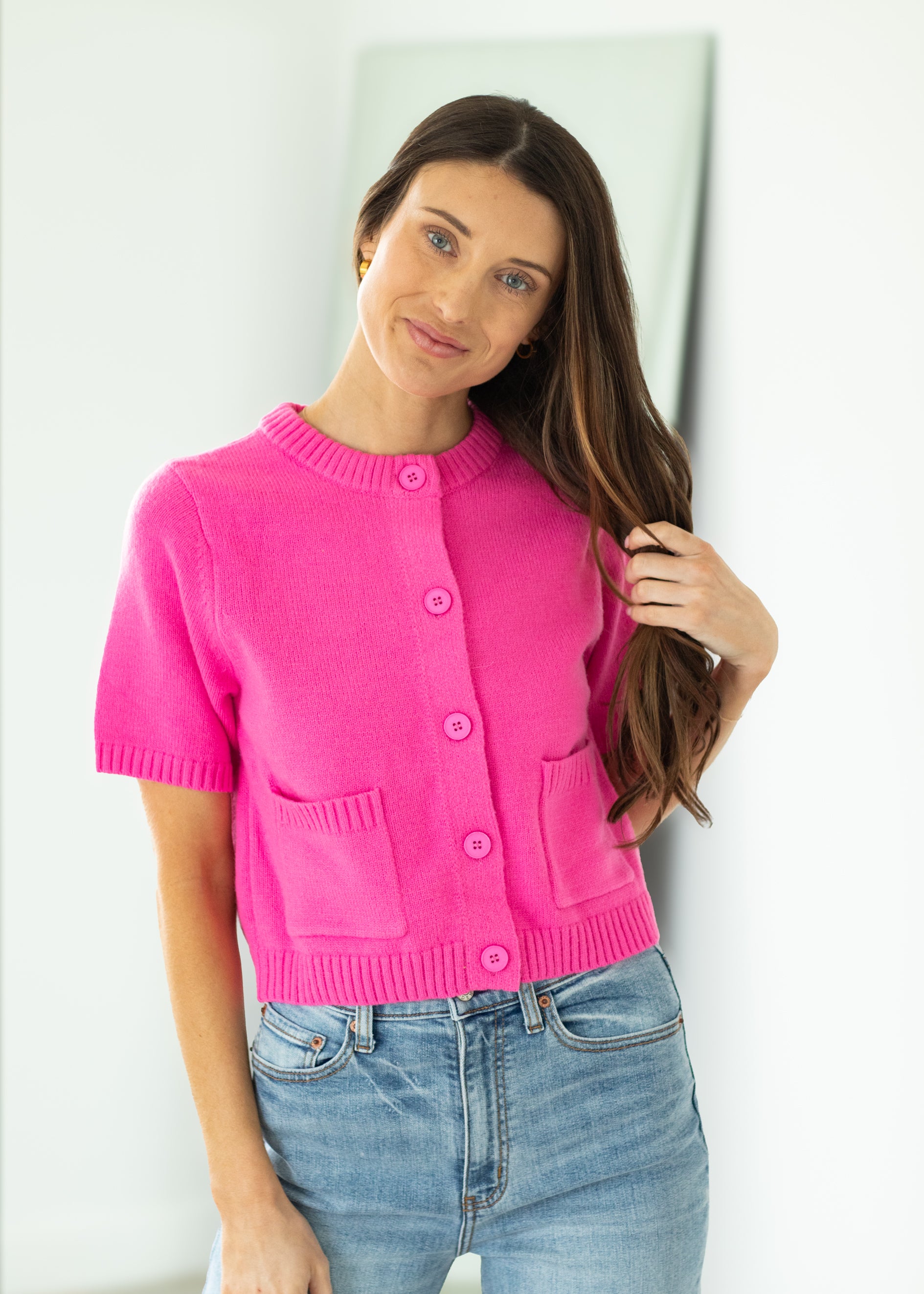 Woman wearing a bright pink cropped cardigan against a beige background

