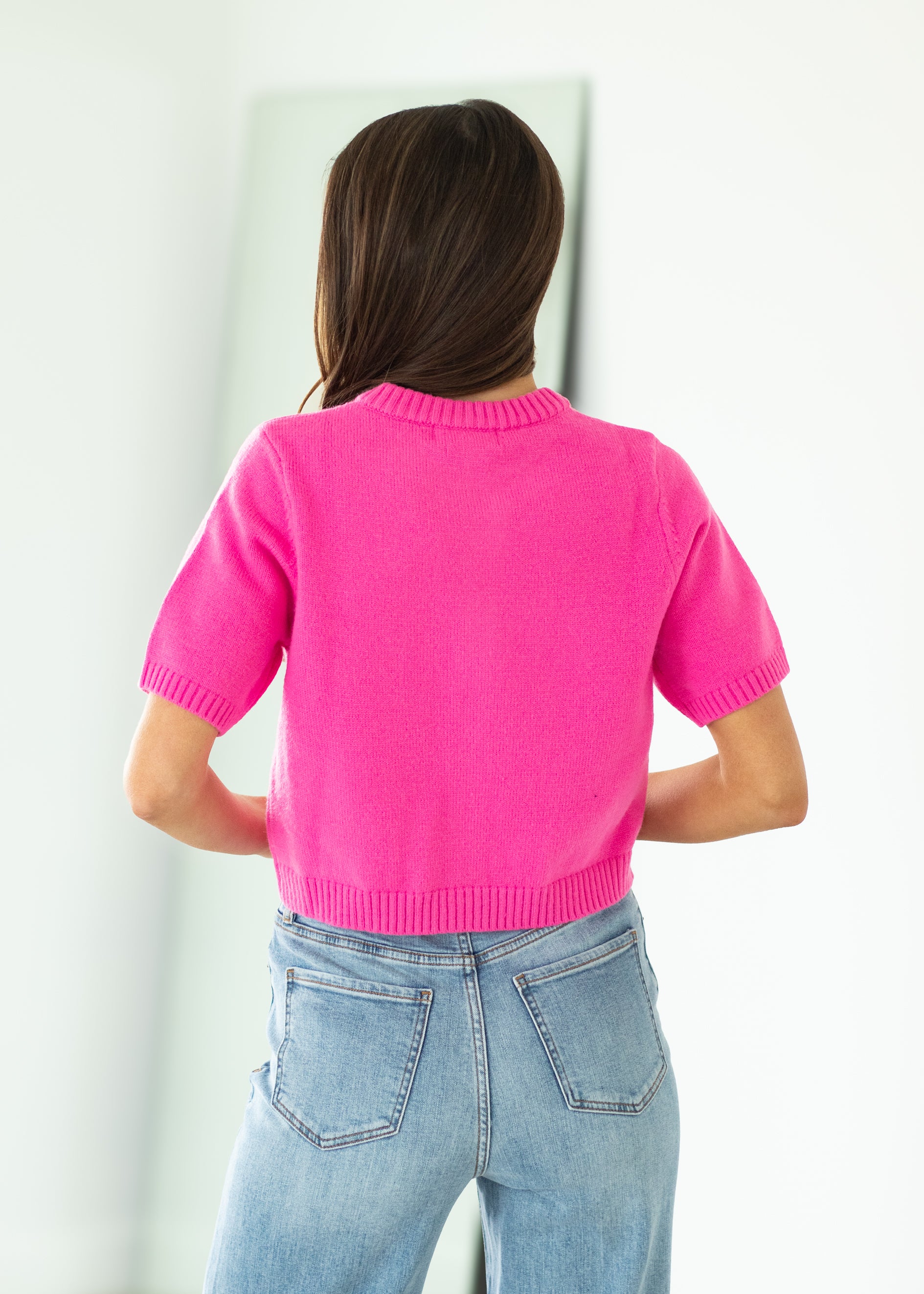 Woman wearing a bright pink cropped cardigan against a beige background

