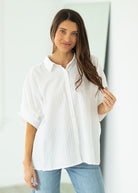 Woman wearing a white oversized shirt and blue jeans against a beige background

