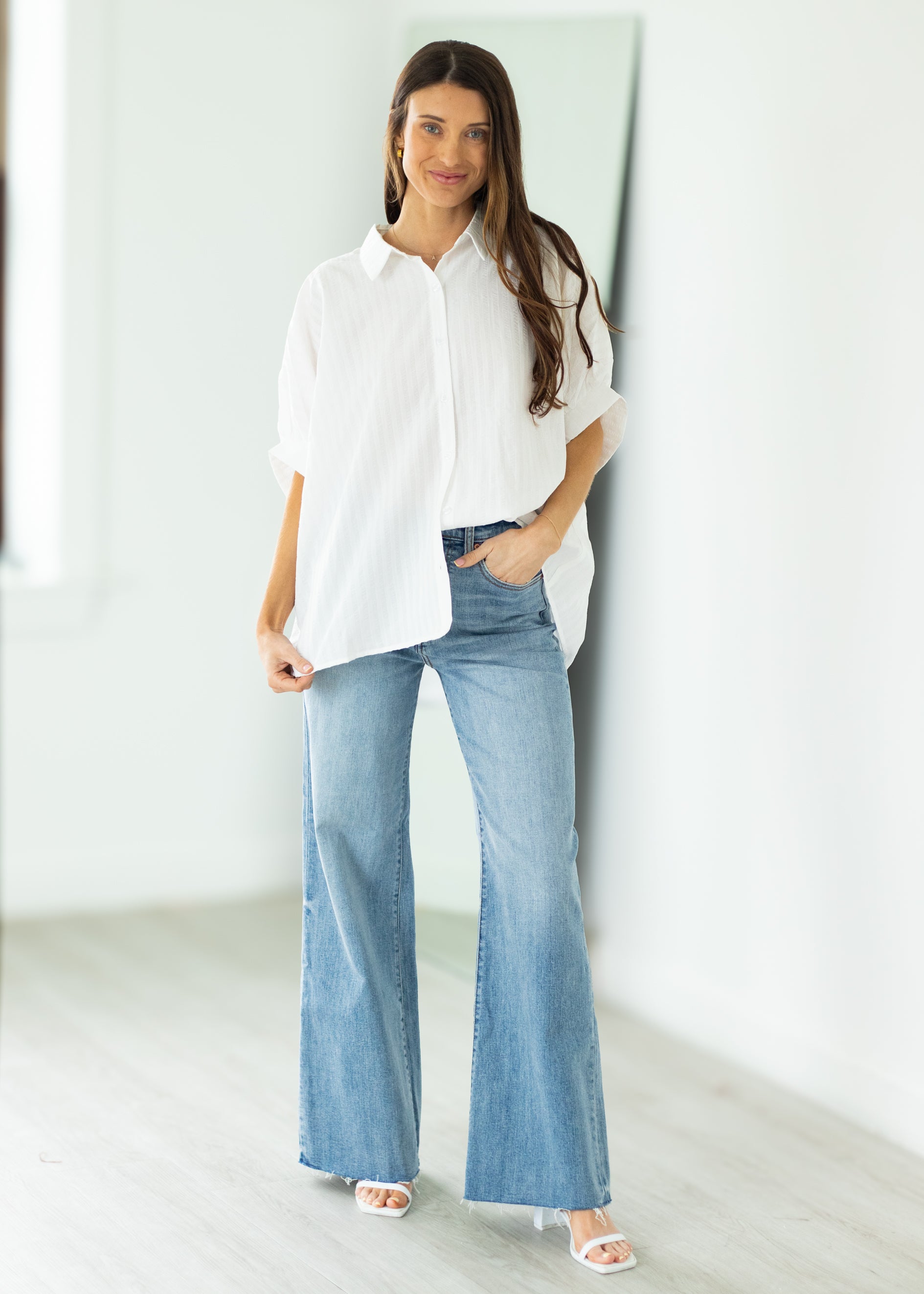 Woman wearing a white oversized shirt and blue jeans against a beige background

