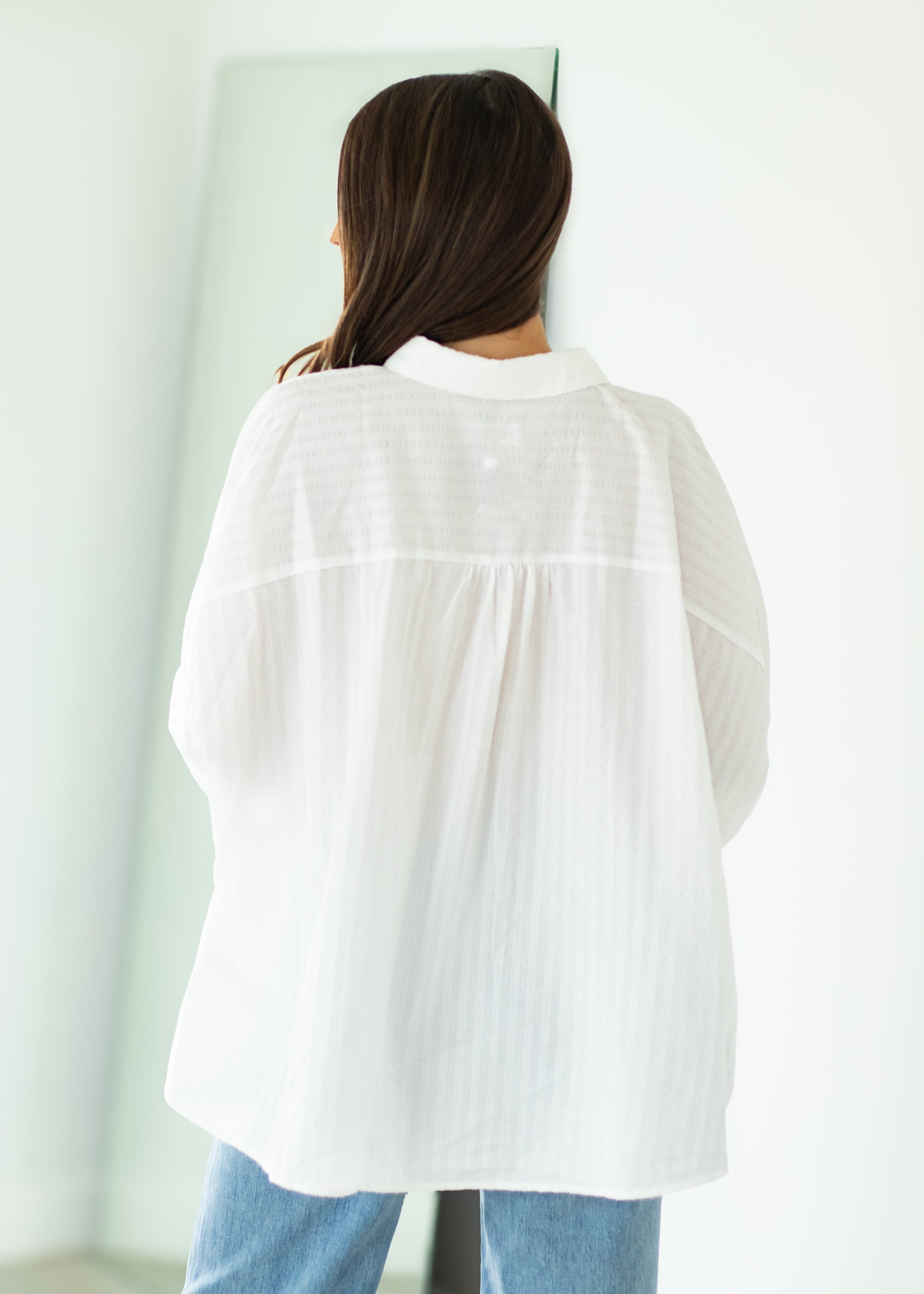 Woman wearing a white oversized shirt and blue jeans against a beige background

