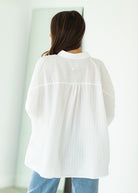 Woman wearing a white oversized shirt and blue jeans against a beige background

