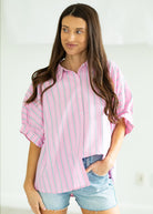 Woman wearing a pink and white striped shirt with denim shorts on a beige background

