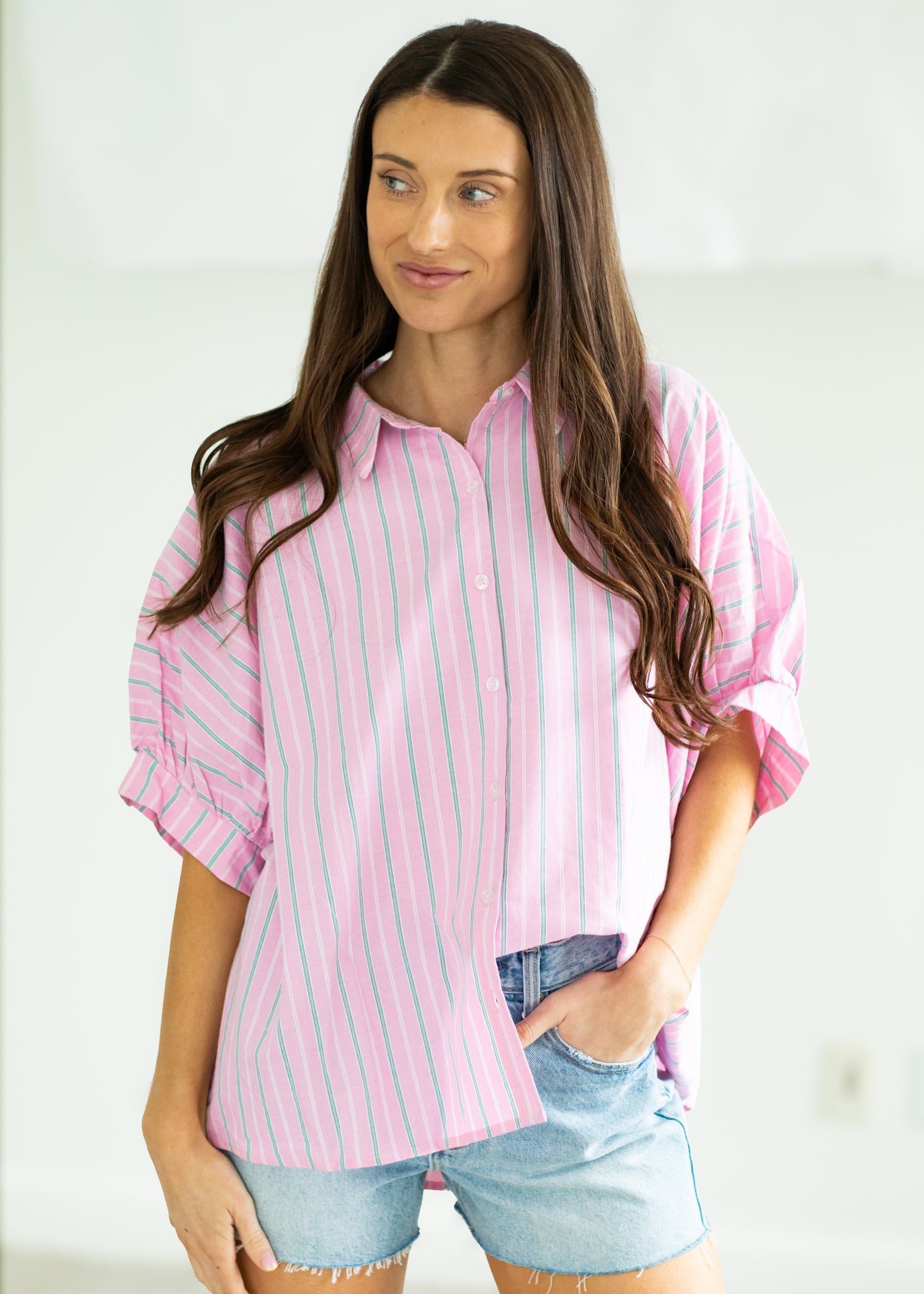 Woman wearing a pink and white striped shirt with denim shorts on a beige background

