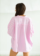 Woman wearing a pink and white striped shirt with denim shorts on a beige background

