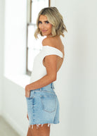 Woman wearing a white off-shoulder top and cream pants against a beige background

