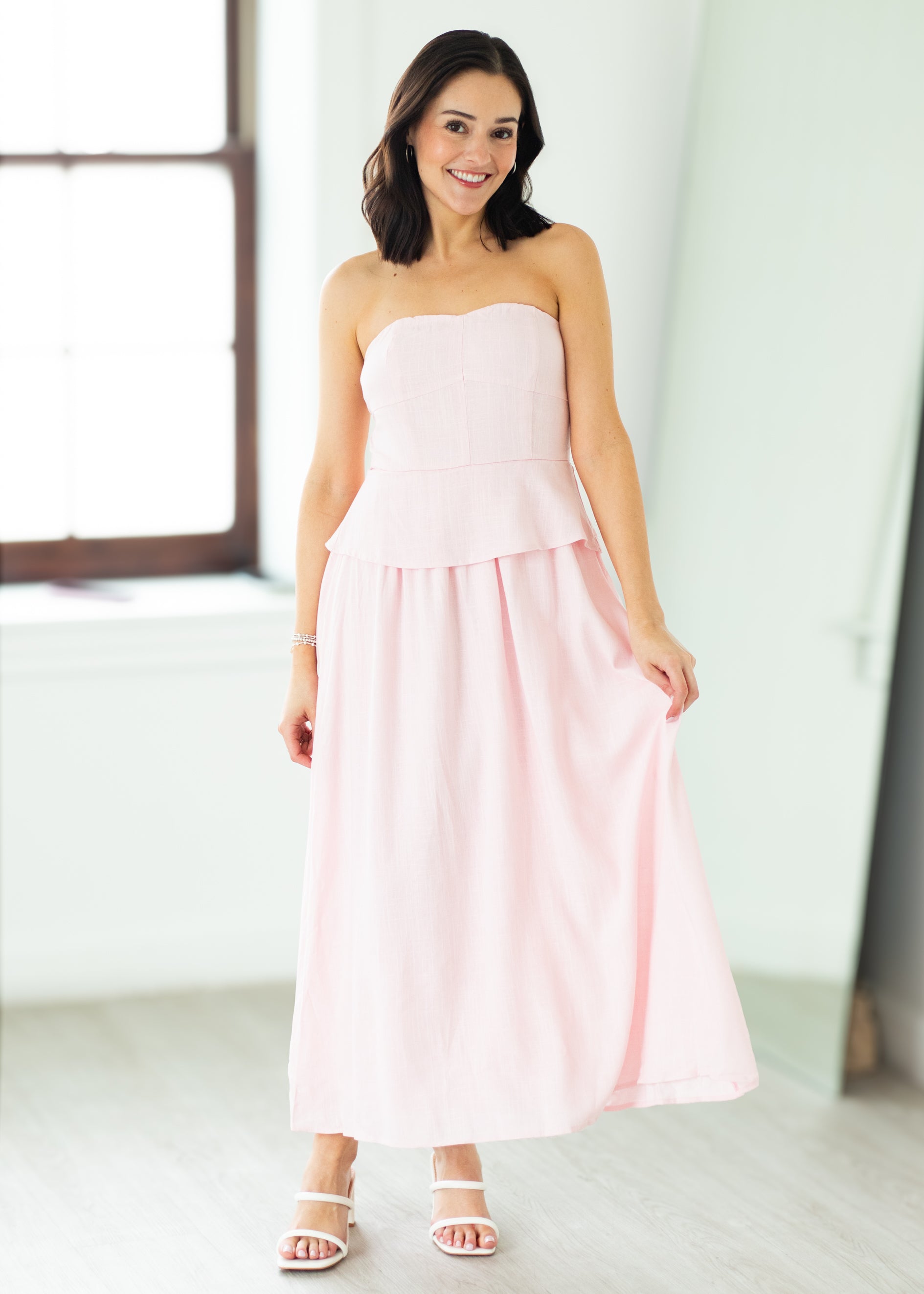 Woman wearing a pink strapless dress with a peplum top on a beige background

