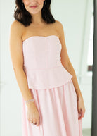 Woman wearing a pink strapless dress with a peplum top on a beige background

