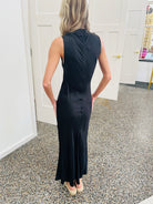 Woman wearing a black sleeveless dress standing in a room with white walls and a speckled floor.