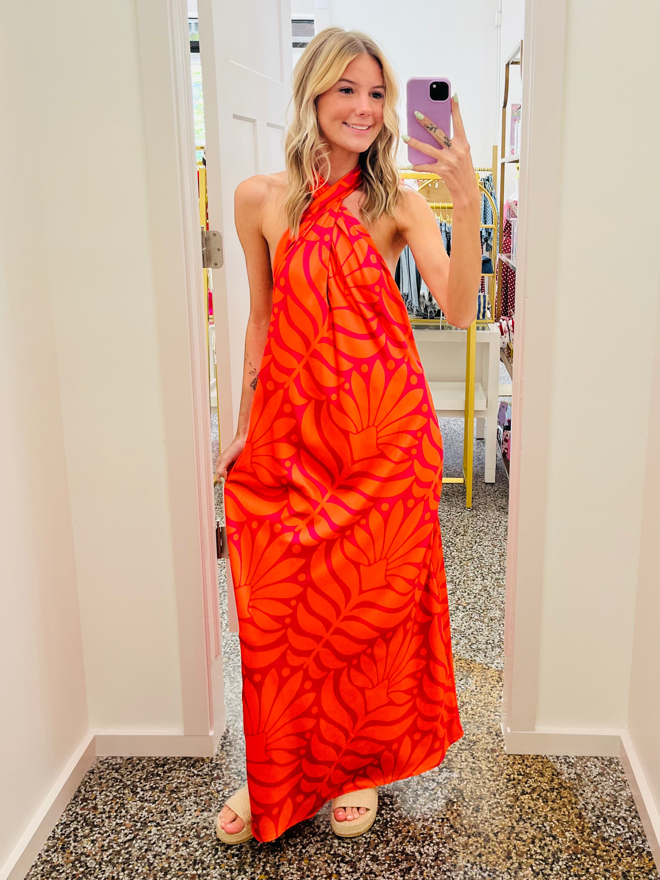 Woman wearing a bright orange halter neck dress with pink patterns, standing in a room.