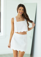 Woman wearing a white outfit with scalloped edges on a gray background

