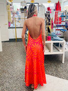 Woman wearing a bright orange dress with a sunflower pattern in a store setting.