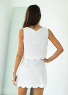 Woman wearing a white outfit with scalloped edges on a gray background

