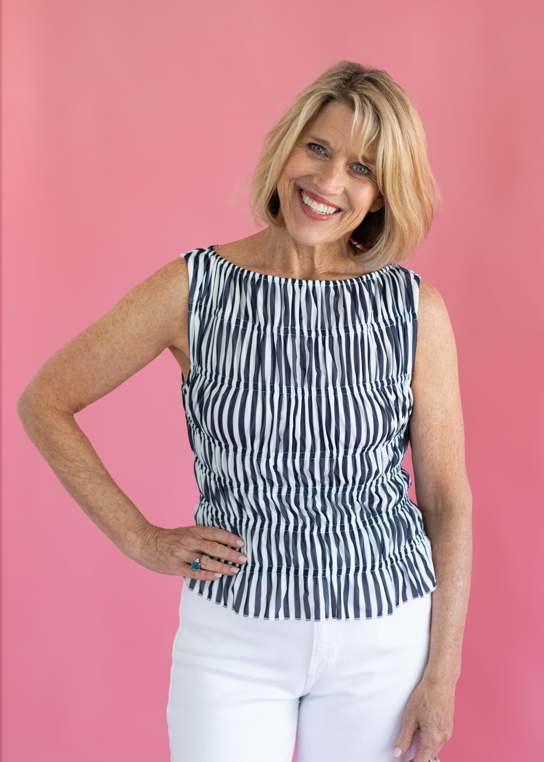 Woman wearing a black and white striped sleeveless top against a pink background