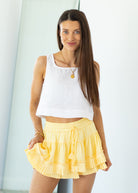 Woman wearing a white top and yellow skirt against a light background