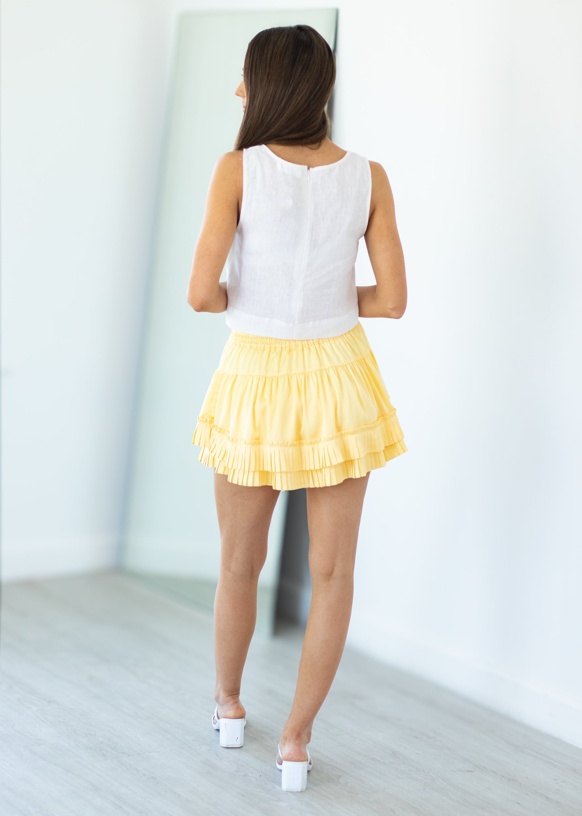 Woman wearing a white top and yellow skirt in a minimalistic setting