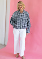 Woman wearing a black and white checkered shirt and white pants against a pink background