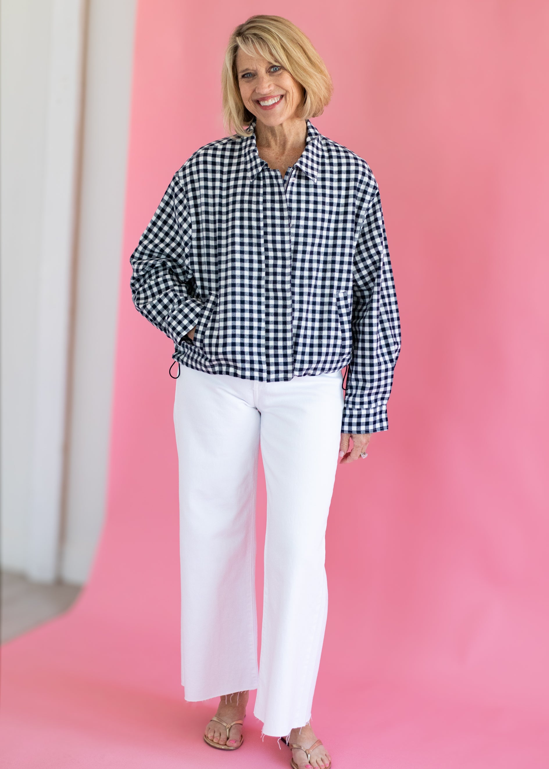 Woman wearing a black and white checkered shirt and white pants against a pink background