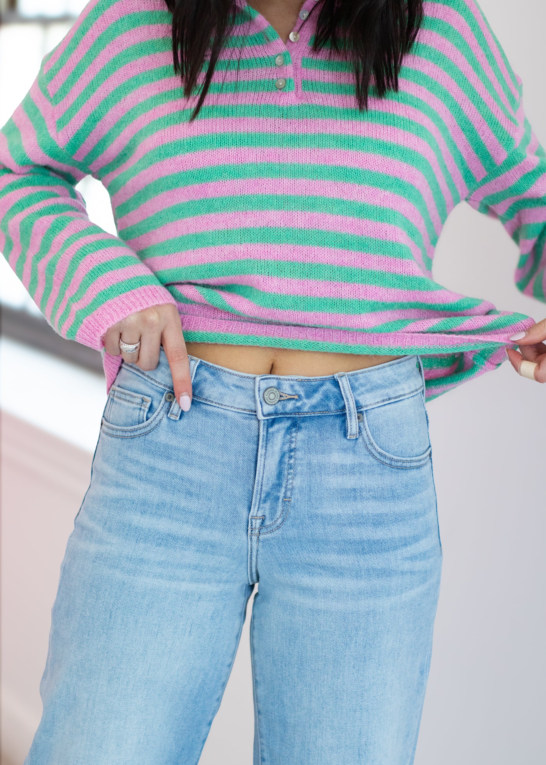 Person wearing a pink and green striped sweater and light blue jeans.