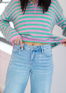 Person wearing a pink and green striped sweater and light blue jeans.