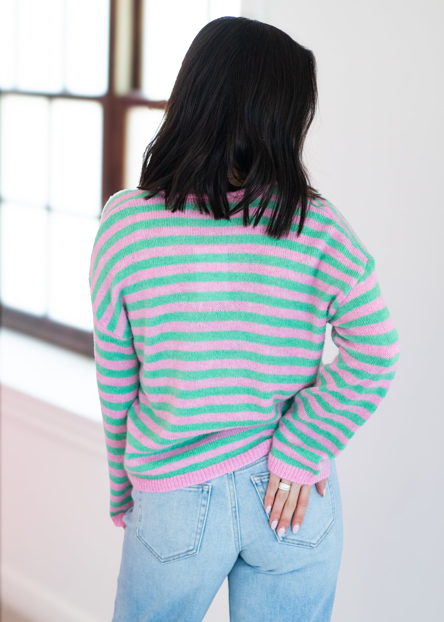Person wearing a pink and green striped sweater with light blue jeans indoors.